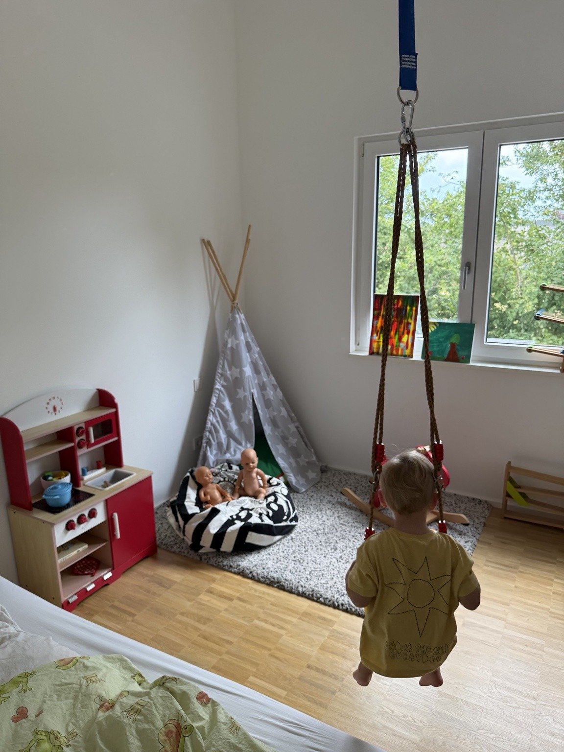 Kind schaukelt im Spielbereich der Kindertagespflege in Eisingen, daneben Spielküche und Kuschelzelt